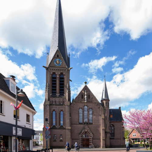 Katholieke kerk aan de Grotestraat in Borne met hoge kerktoren onder een blauwe lucht.