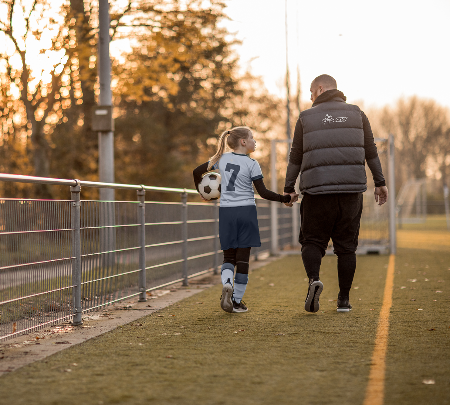 Samenwerking met SVZW Jeugdspeler en begeleider lopen langs de zijlijn van een voetbalveld.
